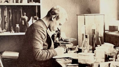 Fridtjof Nansen sitter ved mikroskopet, omgitt av glasskolber med slimål i formalin