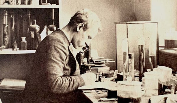 Fridtjof Nansen sitter ved mikroskopet, omgitt av glasskolber med slimål i formalin