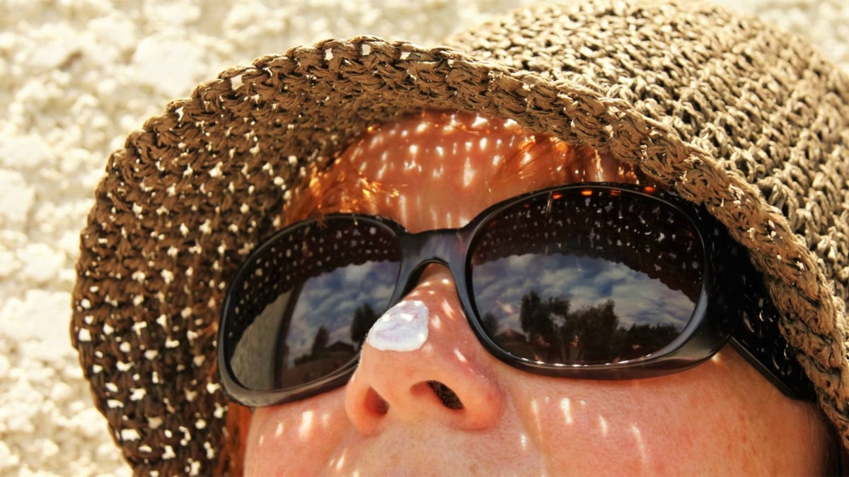 Bilde av dame med solhatt, solbriller og solkrem på nesen